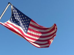 Die wehende, amerikanische Flagge vor blauem Himmel.