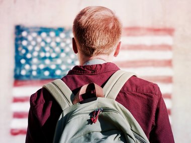 USA Green Card: Ein junger Mann mit einem Rucksack blickt in der Ferne auf eine amerianische Flagge.