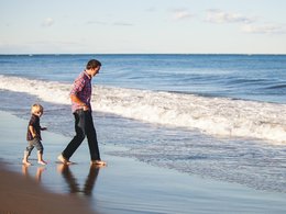 Ein Vater spielt sorgenfrei mit seinem Kind am Strand.