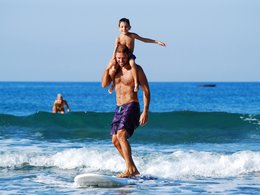 Ein Vater trägt seinen Sohn am Strand auf den Schultern.