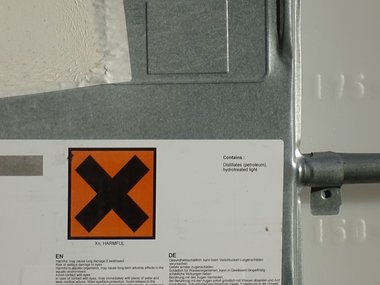 Ein orangenes Zeichen mit einem schwarzen Kreuz an einer Heizungsanlage dient der Warnung vor Gesundheitsschäden.