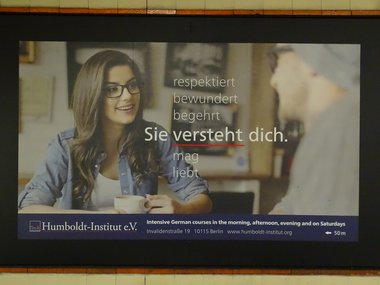 Eine Werbeplakat vom Humboldt-Institut mit einer jungen Frau und den Worten: respektiert, bewundert, begehrt - Sie versteht dich, in einer U-Bahnstation.