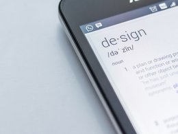 Ein Handy mit einem Whatsapp-Zeichen zeigt eine Seite mit dem Begriff Design in einem Lexikon.