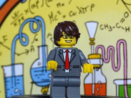 Wirtschaftschemiker - Das Bild zeigt ein Lego-Männchen im Anzug vor einem Chemielabor.