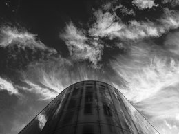 Ein gläserner Wolkenkratzer vor einem aufgewühlten Wolkenhimmel symbolisiert eine Firmenkrise oder Insolvenz.