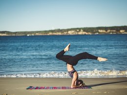 Eine Frau macht einen Yogakopfstand auf einer Decke am Strand.