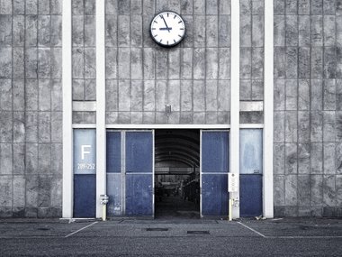 Eine Uhr zeigt kurz vor neun und hängt über einem Tor einer Firma.